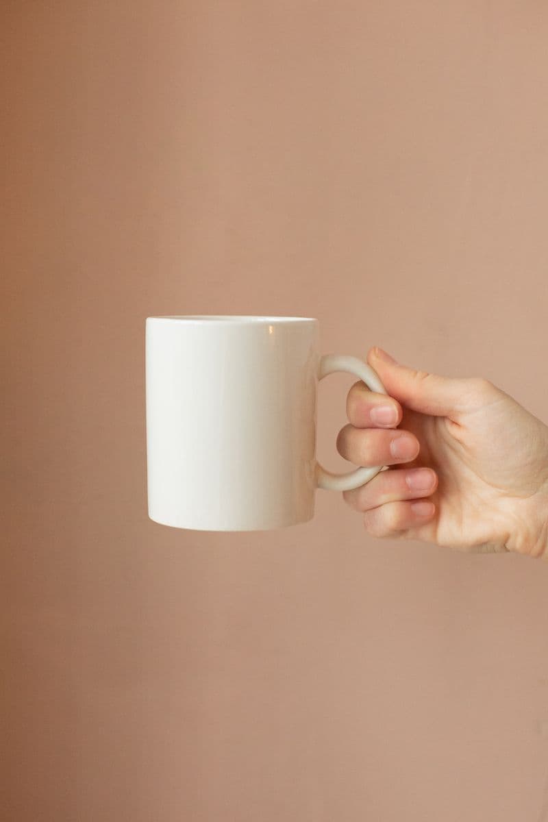 Hand holding a plain white ceramic mug, a finished drinkware goodie.